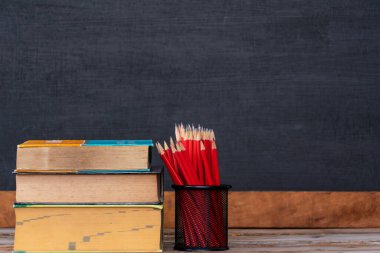 Defterler istiflenmiş ve kalem tutacaklarının masanın üzerine yerleştirilmiş bir sürü kırmızı tahta kalemleri var. Arka plan bir karatahta, okula dönüş konsepti..