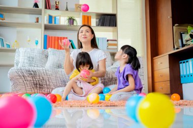 Asyalı bir anne ve kızı renkli toplarla oynuyorlar.