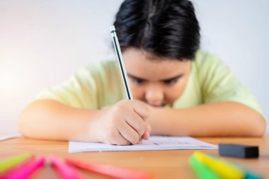 Asyalı çocuklar egzersizleri kararlılıkla çalışıyorlar. Çalışma materyalleri üzerine yazmak için bir kalem kullanıyor..