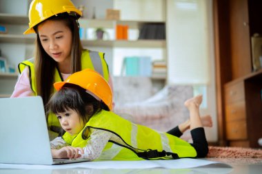 Asyalı anne ve kız tamirci elbisesi giyiyorlar. Öğretim aracı olarak tablet kullanarak öğrenme ve öğrenme