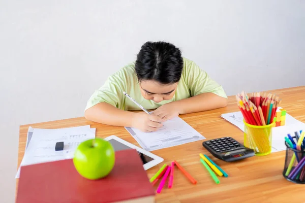Asian children are studying exercises with determination. On the study desk there is study equipment, stationery