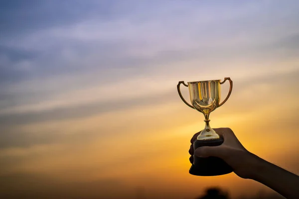 Business hold a trophy showing success until receiving the award. Champion golden trophy for winner, Evening sky background