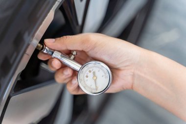 Bir kişi lastik basınç göstergesi kullanarak arabanın lastik basıncını kontrol ediyor. Kişi bir elinde lastik basıncı göstergesini tutuyor ve lastiğin gövdesine bastırıyor..