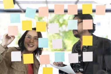 İş adamları ofiste toplanıyor ve fikirleri paylaşmak için notlar kullanıyorlar, beyin fırtınası fikirleri, cam duvardaki yapışkan notlar. İş adamları ofisteki cam duvarda yapışkan notlar okuyorlar..