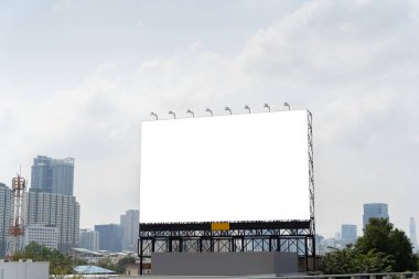 Görüntü, şehir manzarasının ortasında büyük boş bir ilan panosunu gösteriyor. Arka planda uzun binalar ve trafik görülebilir. Reklamcılık ve görsel iletişimin gücü. Kesme yolu.