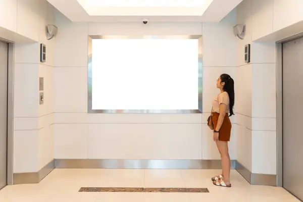 A woman reads an advertisement for a new product on an elevator screen. The woman is intrigued by the ad and considers buying the product. The ad is well-designed and effectively targets its audience.