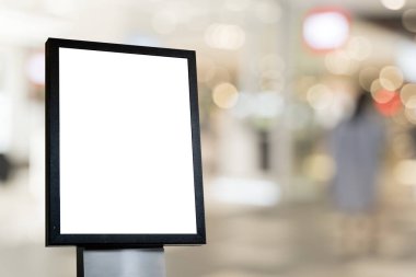 Bulanık alışveriş merkezi arka planında izole edilmiş siyah çerçeveli boş tabela modeli, pazarlama, markalaşma ve yaratıcı tasarım sunumları için boş reklam veya tanıtım panosu şablonu.