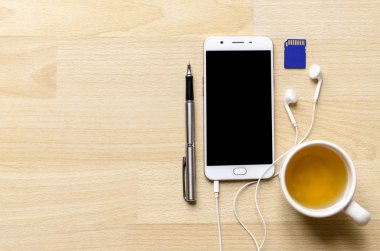 Boş ekran smartphone ile ahşap masa üst üzerinde kulaklık var kalem çay sd adaptörü