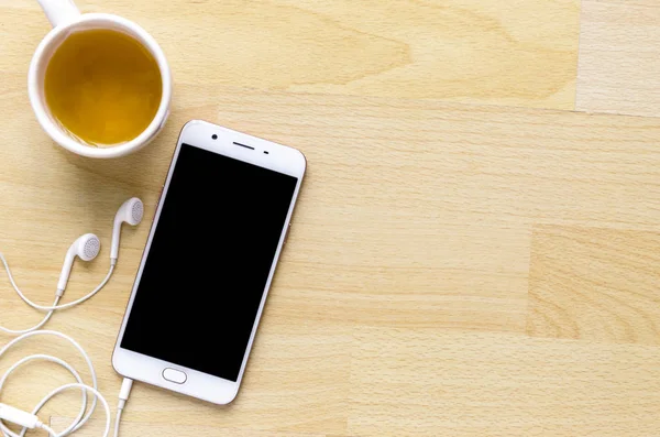 空白屏幕智能手机与耳机在木桌上角有笔茶 适配器 — 图库照片
