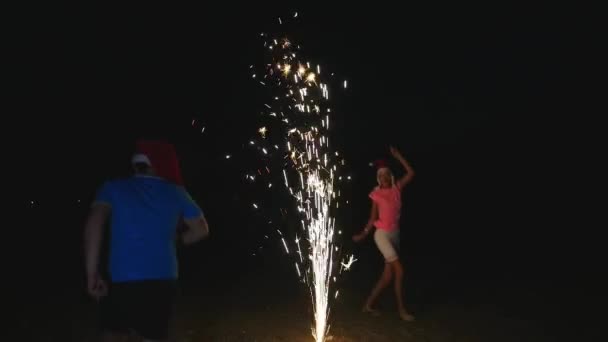 Young man and woman in Christmas hats runnig fireworks fountain sparks around — Stock Video