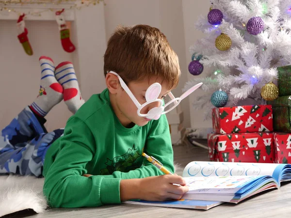 Fiú, vicces szemüveg nem a házi feladatot a karácsonyfa közelében — Stock Fotó