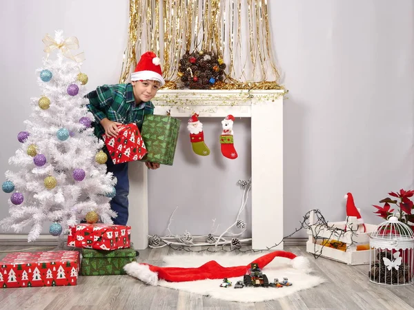 Vicces fiú Santa kalap a karácsonyi fa mögé bújva — Stock Fotó