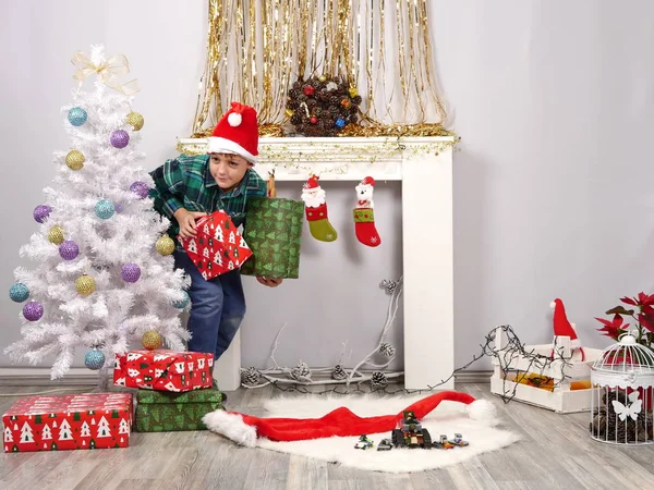 Chico divertido con sombrero de Santa escondido detrás del árbol de Navidad —  Fotos de Stock