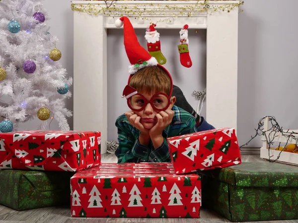 Garçon en chapeau de Père Noël et lunettes de Noël assis derrière les cadeaux de Noël — Photo