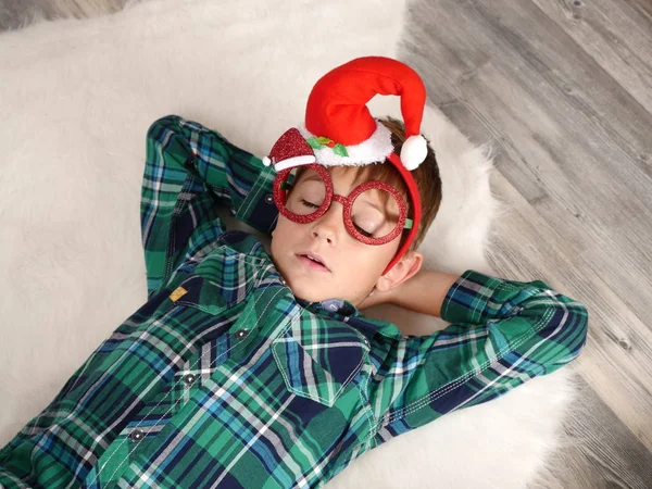 A fiú karácsonyi kalapját, és alszik a szőrme szőnyeg szemüveg — Stock Fotó