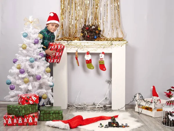 산타 모자 크리스마스 나무 뒤에 숨어있는 재미 있는 소년 — 스톡 사진