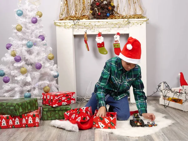 Niño con sombrero de Santa abre regalos cerca del árbol de Navidad —  Fotos de Stock