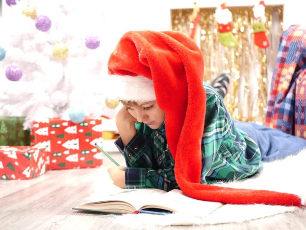Garçon en long chapeau de Noël lisant un livre près du sapin de Noël — Photo