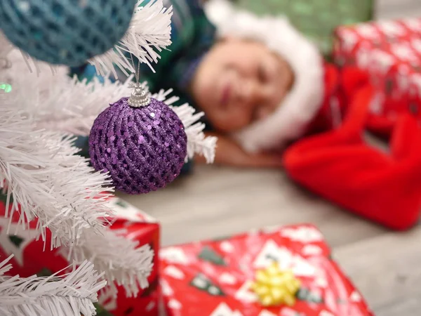 Fiú alszik a földön mögött a karácsonyfa karácsony kalapban — Stock Fotó