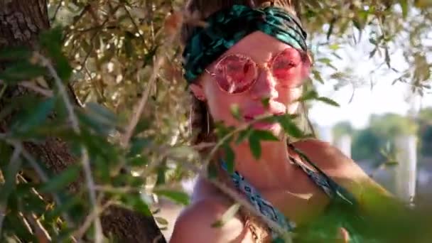 Молода хіпі жінка з сонцезахисними окулярами, що сидять на дереві — стокове відео
