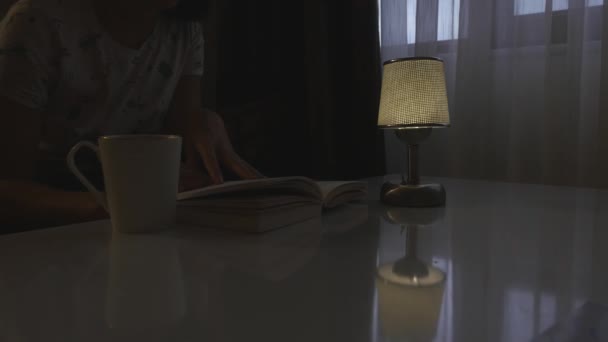 Jeune femme lisant un livre à table le soir — Video