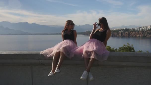 Två vackra unga kvinnor i tyll kjolar och sneakers sitter vid havet — Stockvideo
