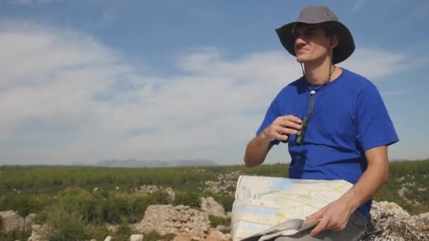 Молодой путешественник с картой, смотрящий далеко через бинокль — стоковое видео