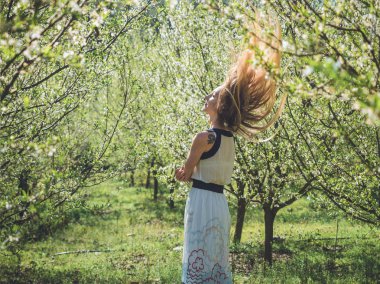 Young beautiful woman with flying long blond hair in spring blossom trees.