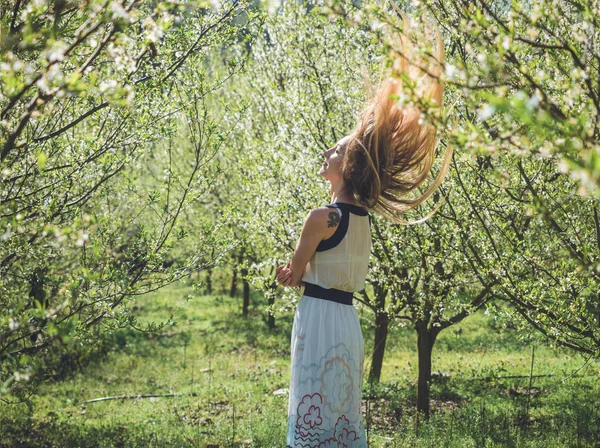 Young beautiful woman with flying long blond hair in spring blossom trees. — Stock Photo, Image