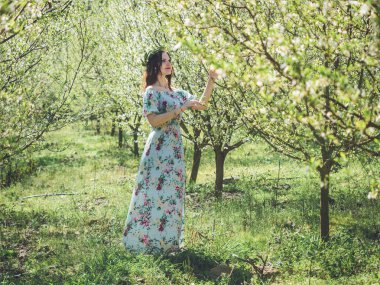 Young beautiful brunette woman in long dress spring blossom trees.