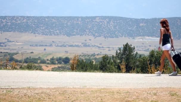 Giovane donna in pantaloncini bianchi va da sola lungo la strada con la valigia — Video Stock