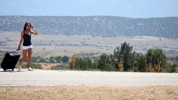 Mladá žena v bílých kraťasech jde sama po silnici s kufrem — Stock video