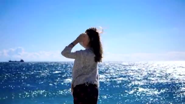 Молодая женщина стоит у моря в ветреную погоду — стоковое видео