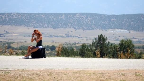 Mladá žena v bílých šortkách sedí na kufru a pak jde po silnici — Stock video