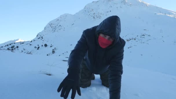 Νεαρός με σκούρα ρούχα να πέφτει εξαντλημένος σε ένα χιονισμένο βουνό — Αρχείο Βίντεο