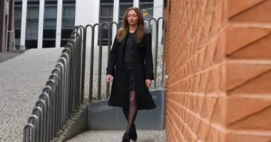 Young woman walking by red brick wall