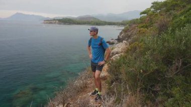 Hiker looking to the beatifull sea view. Young man tourist with a backpack standing on top of a mountain.
