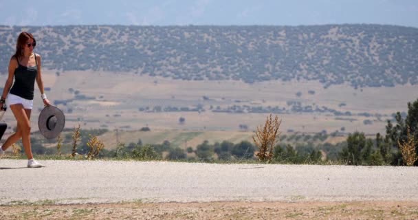 Fiatal nő fehér rövidnadrágban megy egyedül az úton a bőrönddel — Stock videók