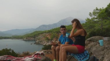 Young couple sitting on rocks in forest eating picnic