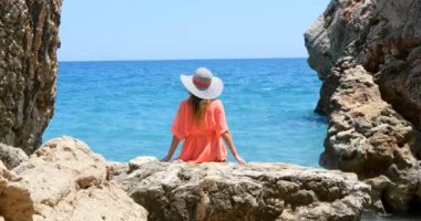 Young pretty woman in swimsuit and coverup sitting on the rocks near the sea