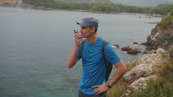 Caminante hablando por la estación de radio. Joven turista con una mochila en la cima de una montaña . — Vídeo de stock