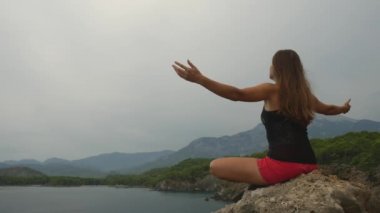 Kadın turist açık gökyüzü ve sakin deniz arka plan üzerinde bir kaya üzerinde oturan