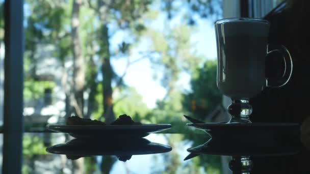 Nierozpoznana sylwetka kobiety siedzącej ze szklanką cappuccino i ciasta — Wideo stockowe