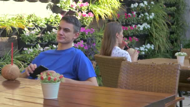 Young man and woman sitting at the table with coconut drink — Stockvideo