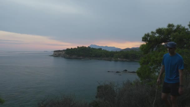 Junges Touristenpaar mit Blick auf den herrlichen Meerblick bei Sonnenuntergang. Touristenpaar mit Rucksack auf einem Berg. — Stockvideo