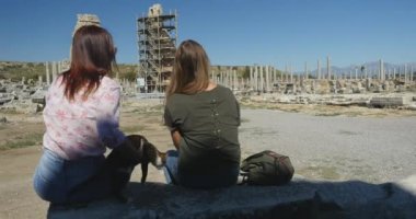Young women watching on ruins, while sitting on the stone in Ancient city Perge, open air antique historical museum