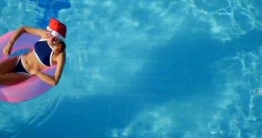 Woman in santa hat relaxing in a pool on the pink inflatable ring