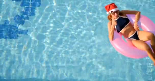 Donna in cappello da Babbo Natale rilassante in piscina sull'anello gonfiabile rosa — Video Stock