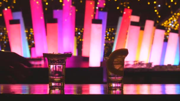 Couple taking two silver tequila shots with lime on bar counter with color changing  led tube lamps — Stock Video