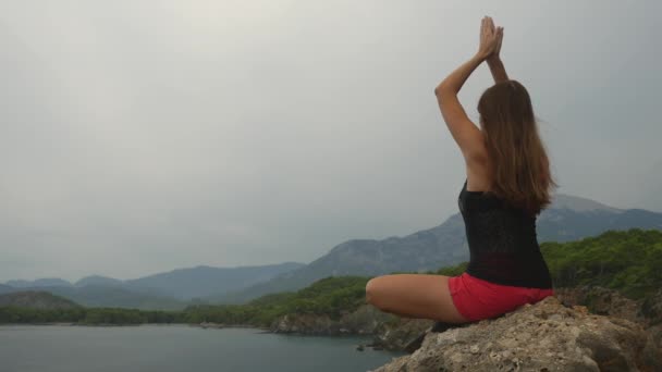 Turista sentada en una roca sobre un cielo despejado y un fondo marino tranquilo — Vídeos de Stock